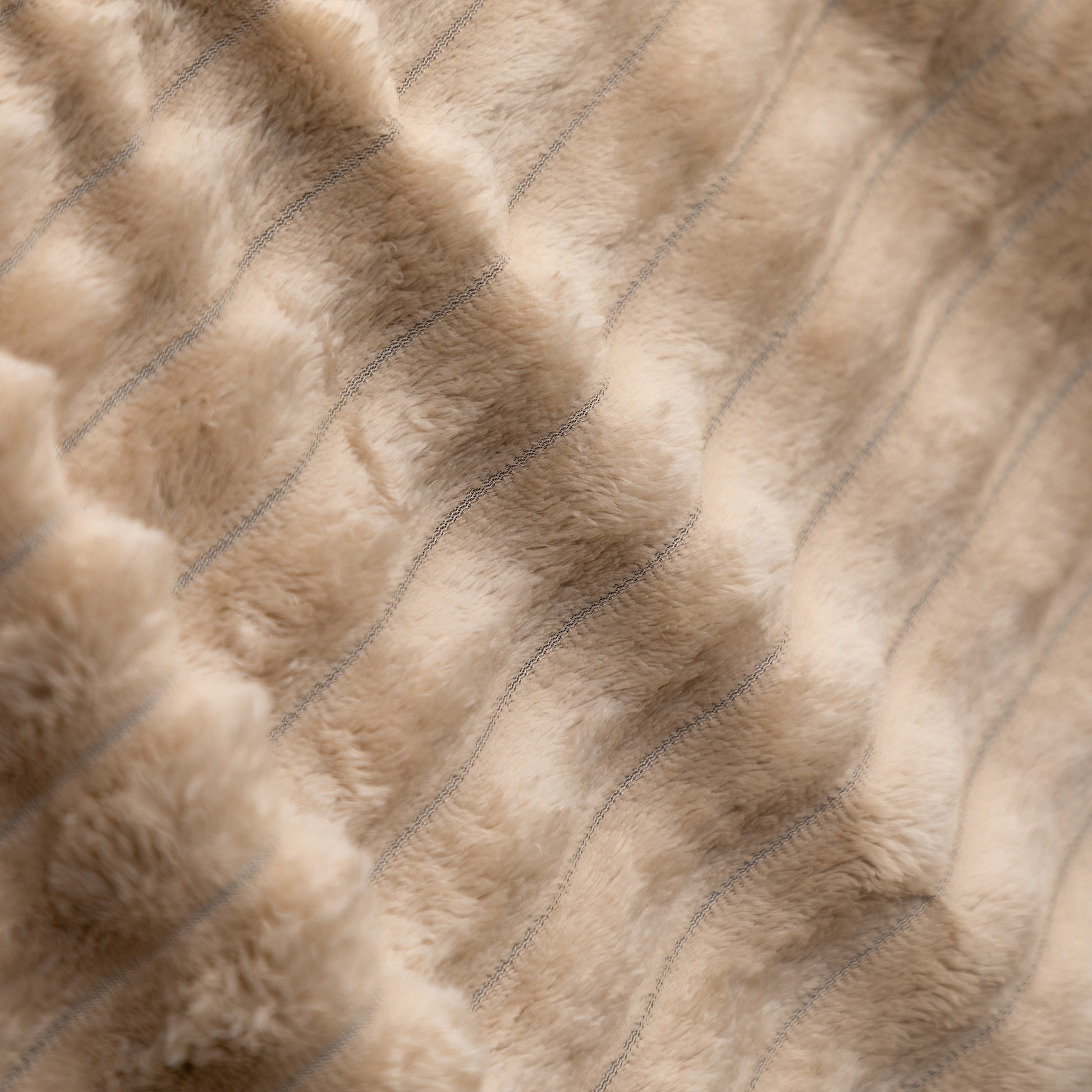 Close-up of a plush faux fur or sheepskin-style textile in a warm beige/taupe tone with subtle stitched vertical channeling.