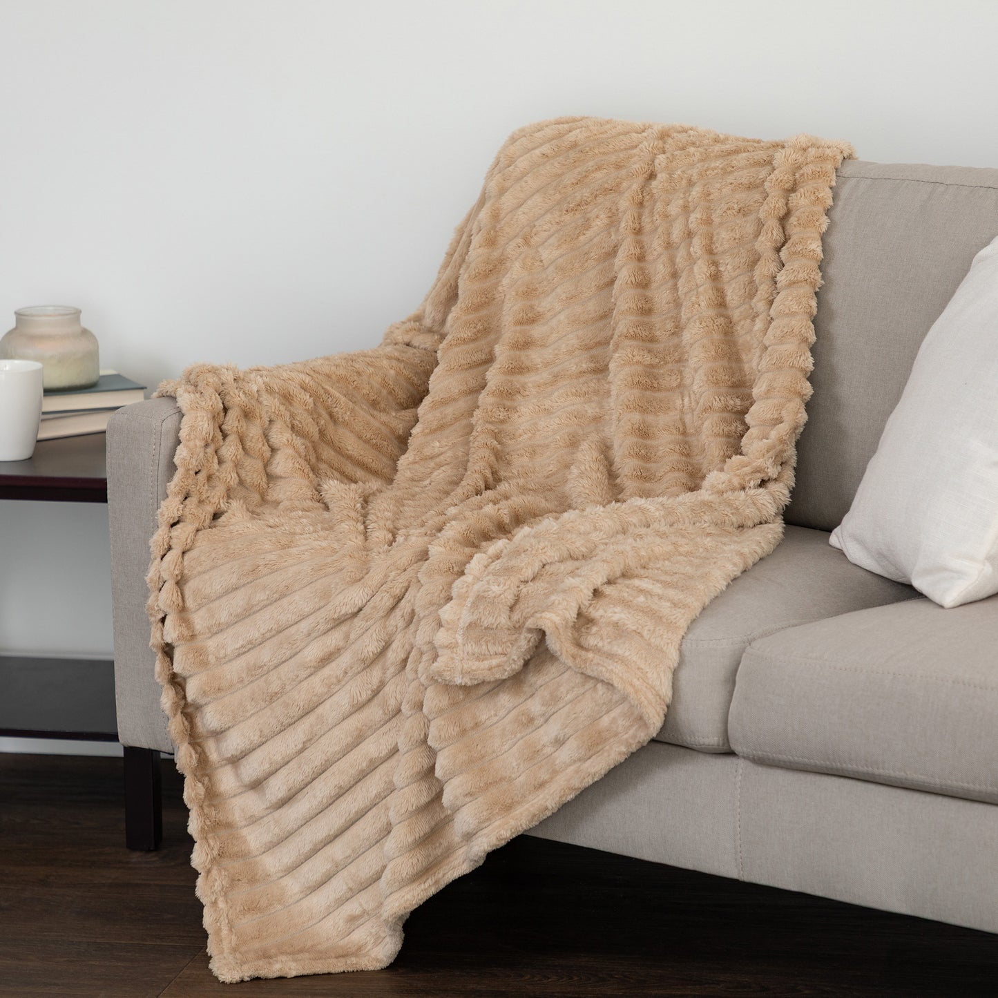 A chunky ribbed faux fur throw blanket in a warm beige/tan color draped over a light gray sofa in a living room setting.