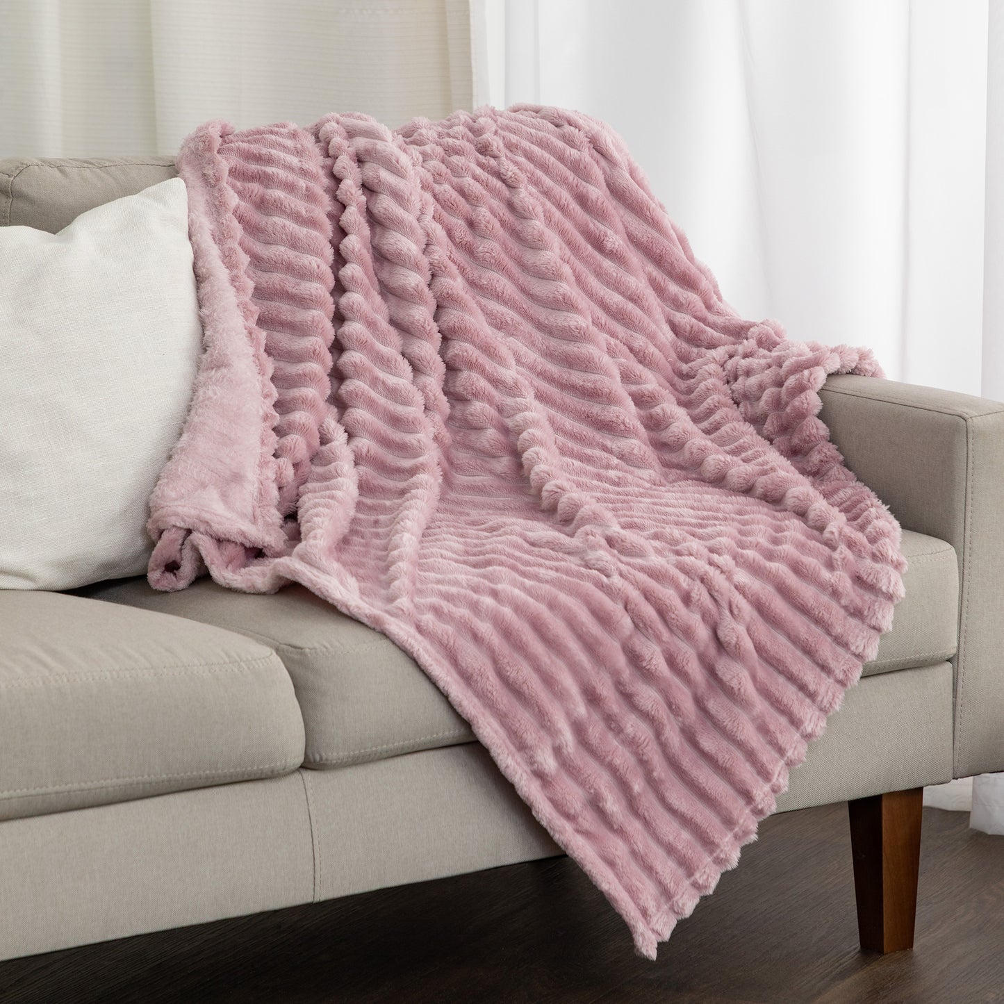 A dusty pink textured throw blanket draped over a light beige sofa in a living room setting.
