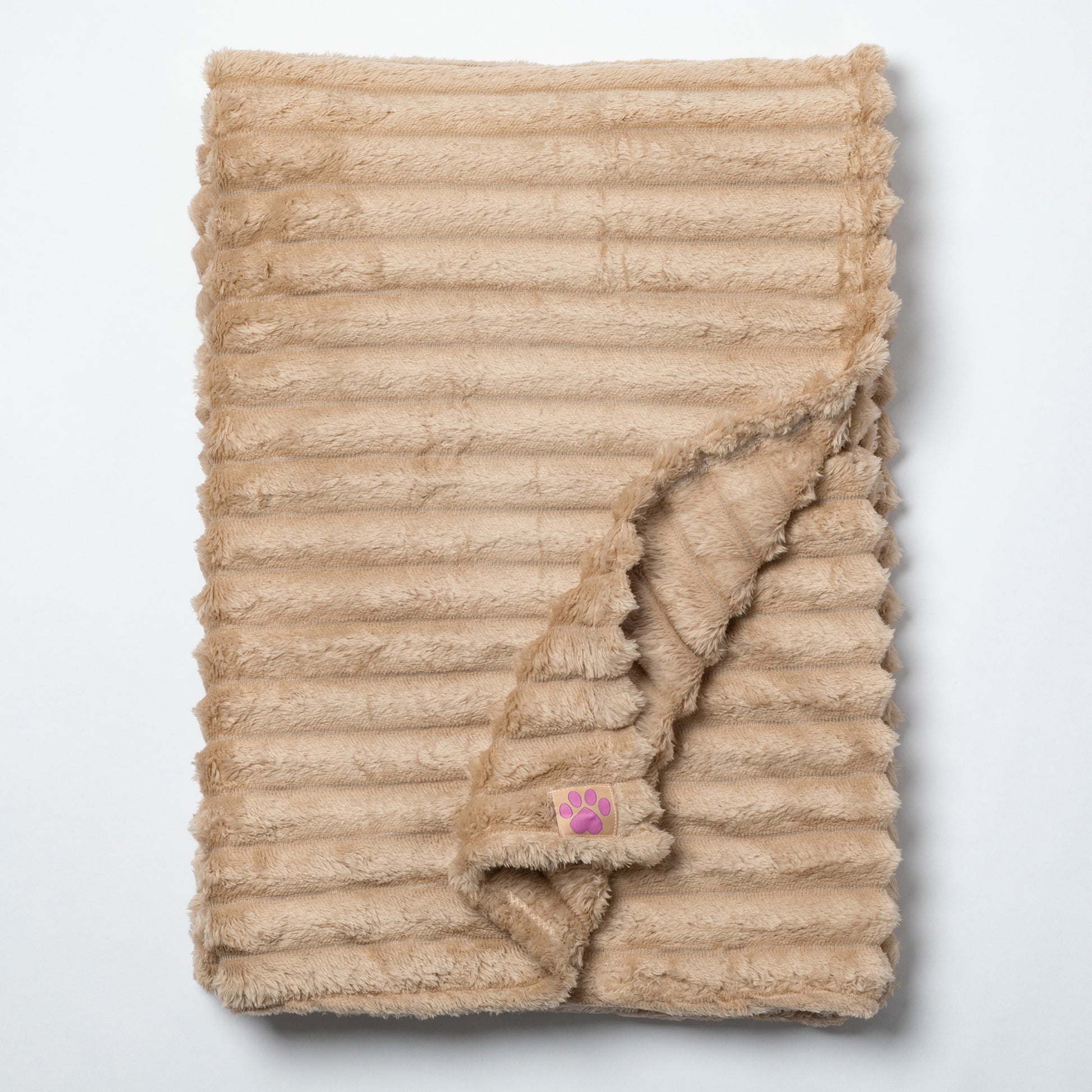 A beige ribbed faux fur blanket with a small pink paw print patch, folded to show its soft texture on a light gray background.