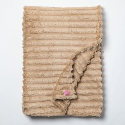 A beige ribbed faux fur blanket with a small pink paw print patch, folded to show its soft texture on a light gray background.