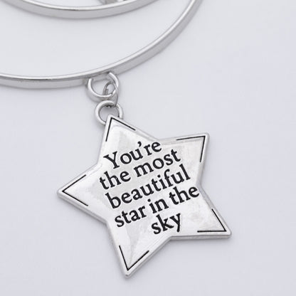 A silver-tone metal keychain featuring a five-pointed star charm engraved with the quote 'You're the most beautiful star in the sky' in black lettering, attached to a matching silver keyring on a light gray background.