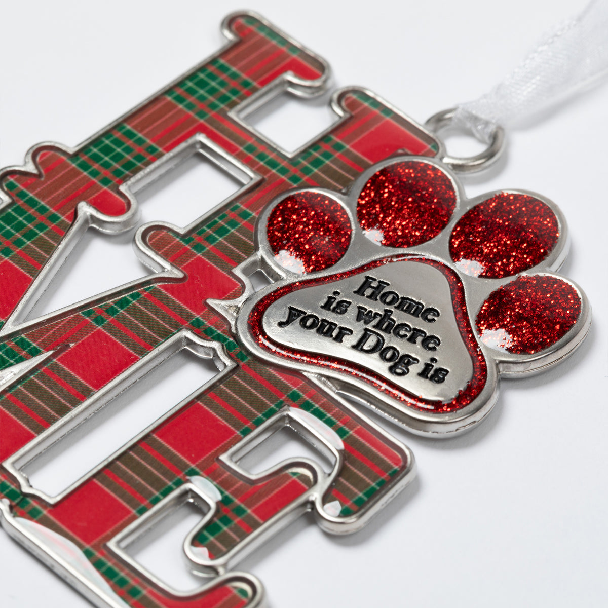 A close-up of a metal Christmas ornament featuring the word 'HOME' in red and green plaid lettering, with a glittery red paw print charm in the center that reads 'Home is where your Dog is' on a white background.