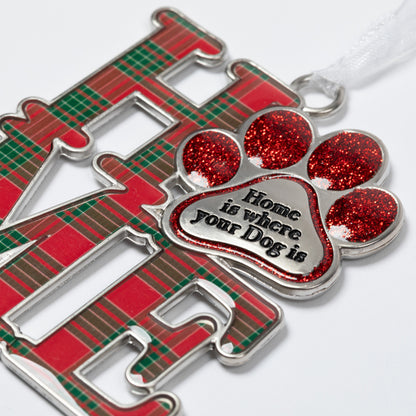 A close-up of a metal Christmas ornament featuring the word 'HOME' in red and green plaid lettering, with a glittery red paw print charm in the center that reads 'Home is where your Dog is' on a white background.