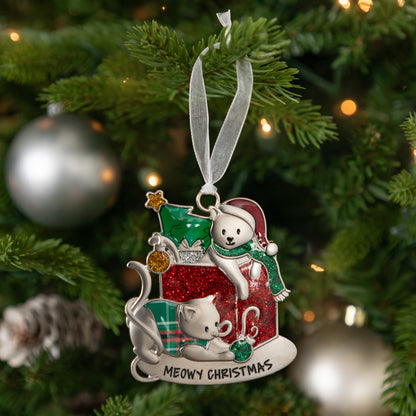 A personalized Christmas ornament with a christmas present featuring two cats, hanging on a green Christmas tree with silver ornaments and warm bokeh lights in the background. The ornament features a silver cat, a white cat, red glitter details, and the text 'MEOWY CHRISTMAS' at the bottom.