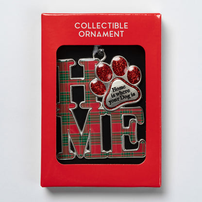 A collectible Christmas ornament displayed inside its red retail packaging. The ornament features the word 'HOME' in large silver letters with a red and green plaid pattern, alongside a red glitter paw print and a silver heart-shaped tag that reads 'Home is where your Dog is'.