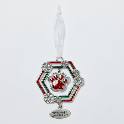 A silver-toned dog ornament featuring a red glitter paw print in the center, surrounded by a red and green glitter hexagonal frame with silver snowflake accents. A white ribbon is tied to the top, and a dangling silver tag at the bottom reads 'All you need is Love and a Dog'.