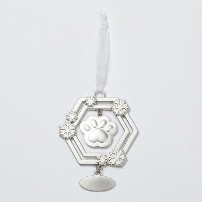 A silver-toned metal pet memorial ornament featuring a central paw print, surrounded by a hexagonal frame with snowflake-like accents and a hanging oval plate, suspended from a white ribbon on a light gray background.