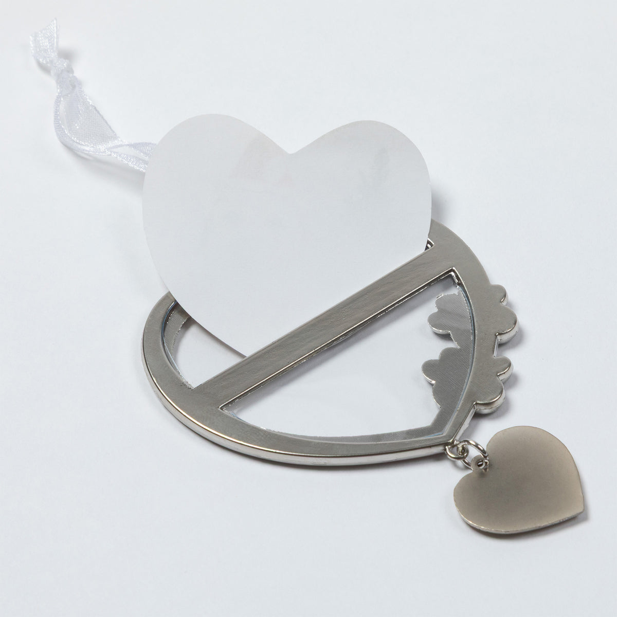 A silver metal heart-shaped keepsake frame with a white heart-shaped card inserted, a white ribbon loop, and a small dangling heart charm, shown on a plain white background.
