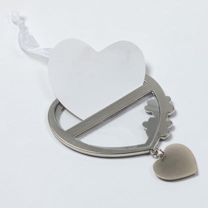 A silver metal heart-shaped keepsake frame with a white heart-shaped card inserted, a white ribbon loop, and a small dangling heart charm, shown on a plain white background.