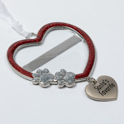 A heart-shaped pet memorial ornament with a red glitter border, silver metal frame, two paw print charms covered in clear rhinestones, and a dangling heart charm engraved with 'Santa's Favorite'.