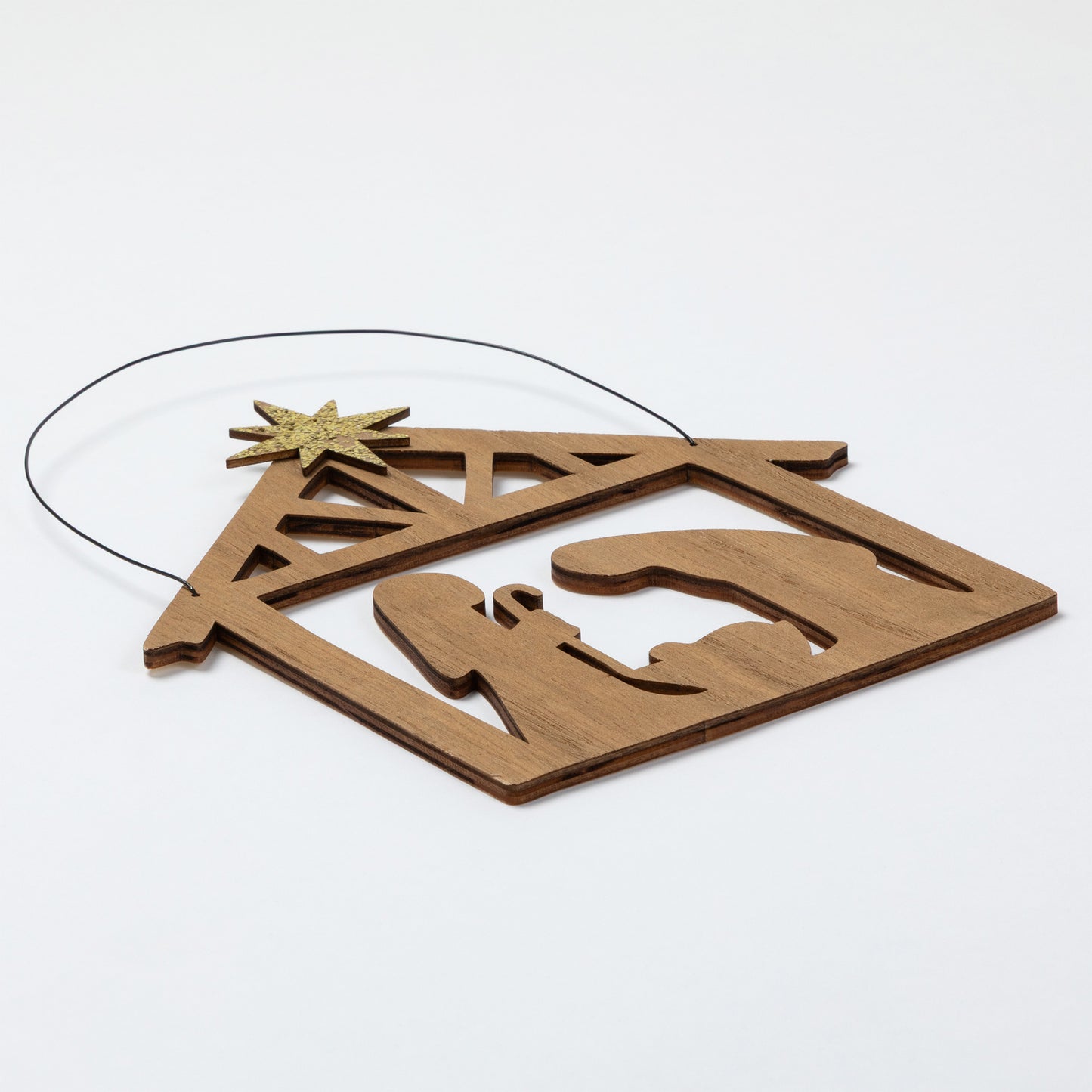 A wooden nativity scene ornament featuring a stable silhouette with a star on top, suspended by a thin black wire against a plain white background.