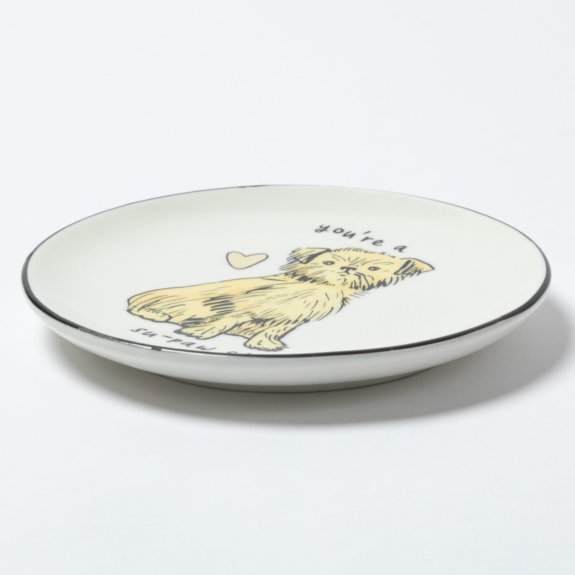 A white ceramic plate with a black rim, featuring a hand-drawn illustration of a yellow dog with the text 'you're a' above it and 'in love' below it, shown on a clean white background.