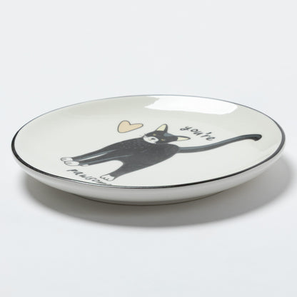 A white ceramic shallow dish with a black rim, featuring a black cat illustration, a small beige heart, and the words 'you're amazing' on a light gray background.