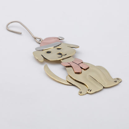 A brass dog-shaped ornament with a pink bow tie and hat, shown on a plain light gray background.
