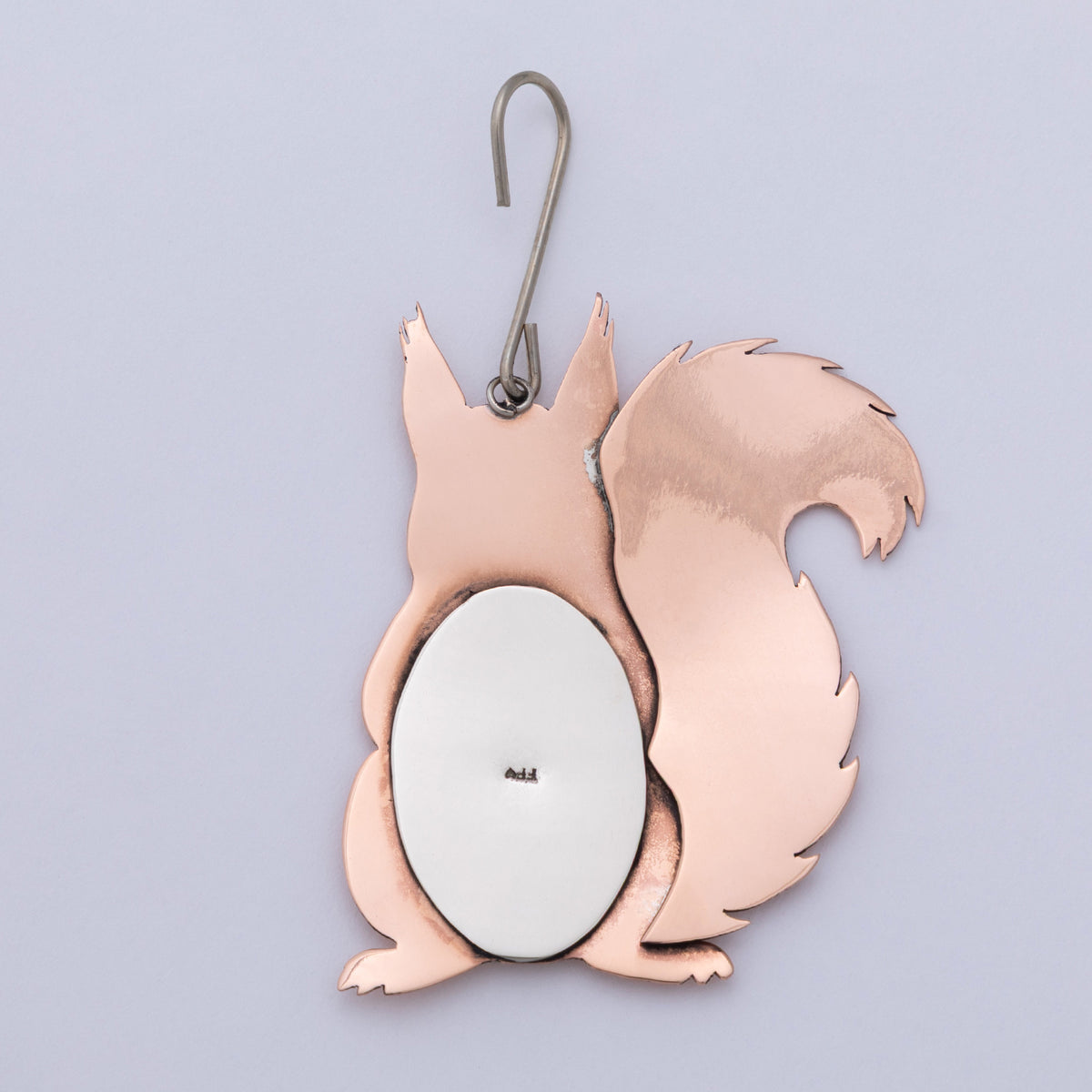 A copper-colored metal squirrel-shaped mirror with a silver metal hanger and a white oval mirror center, shown against a light lavender background.