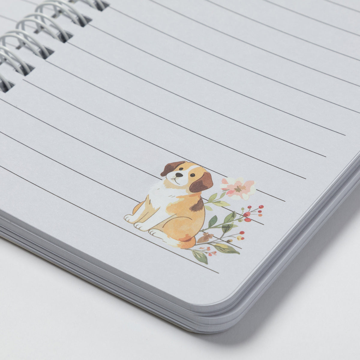 A close-up of a spiral-bound lined notebook with a small watercolor illustration of a dog and flowers on the page.
