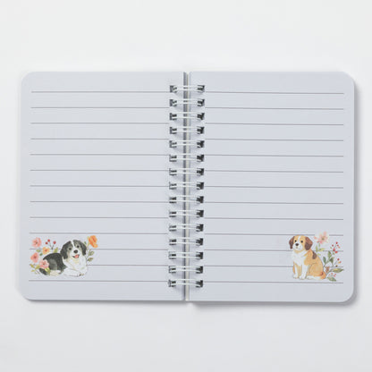 An open spiral-bound lined notebook on a light gray background. The pages are white with horizontal lines, and there are small watercolor illustrations of dogs near the bottom left and bottom right corners.