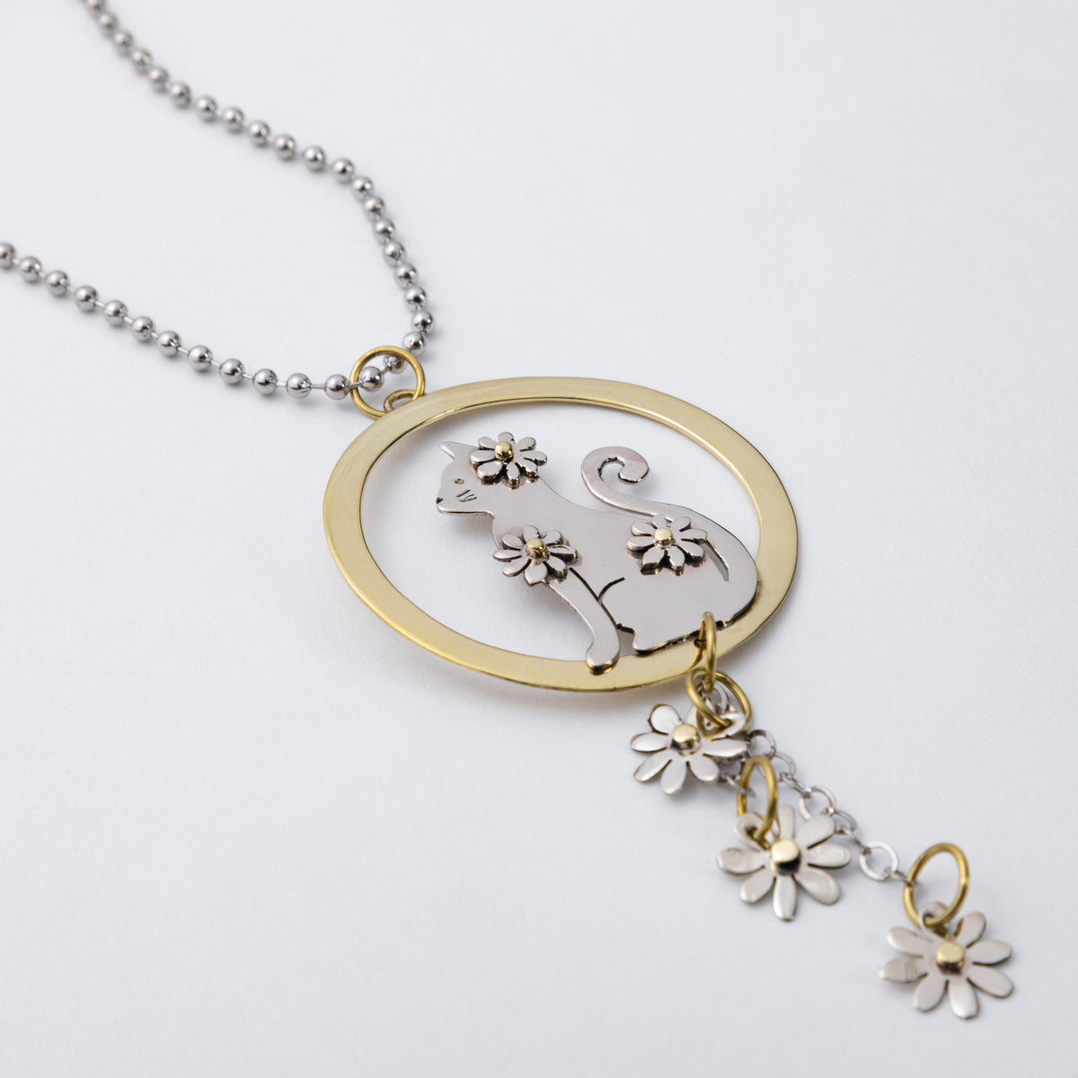 A silver ball chain car charm featuring a circular pendant with a silver cat silhouette and flower details, accented by a gold-tone ring and matching dangling flower charms, shown on a light gray background.