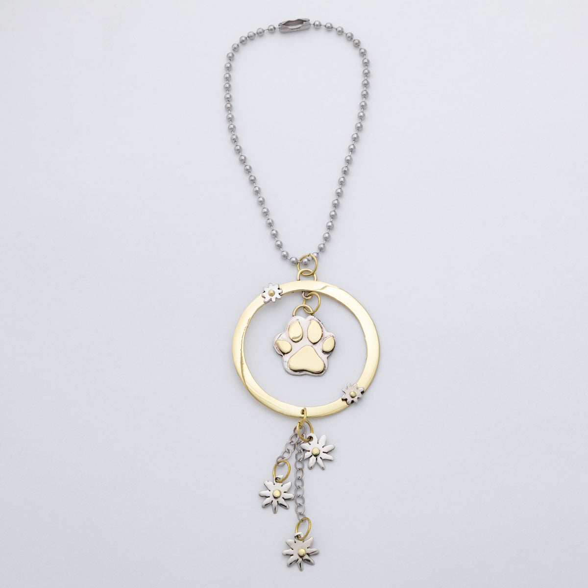 A gold and silver pet memorial necklace featuring a circular pendant with a paw print charm and dangling flower charms, shown on a light gray background.