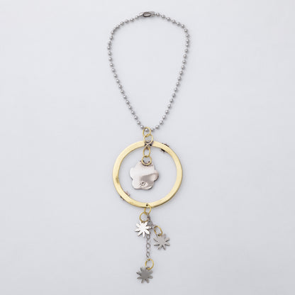 A silver-toned beaded necklace with a gold-toned circular frame and a central silver flower charm, featuring three dangling star and leaf charms, shown on a light gray background.