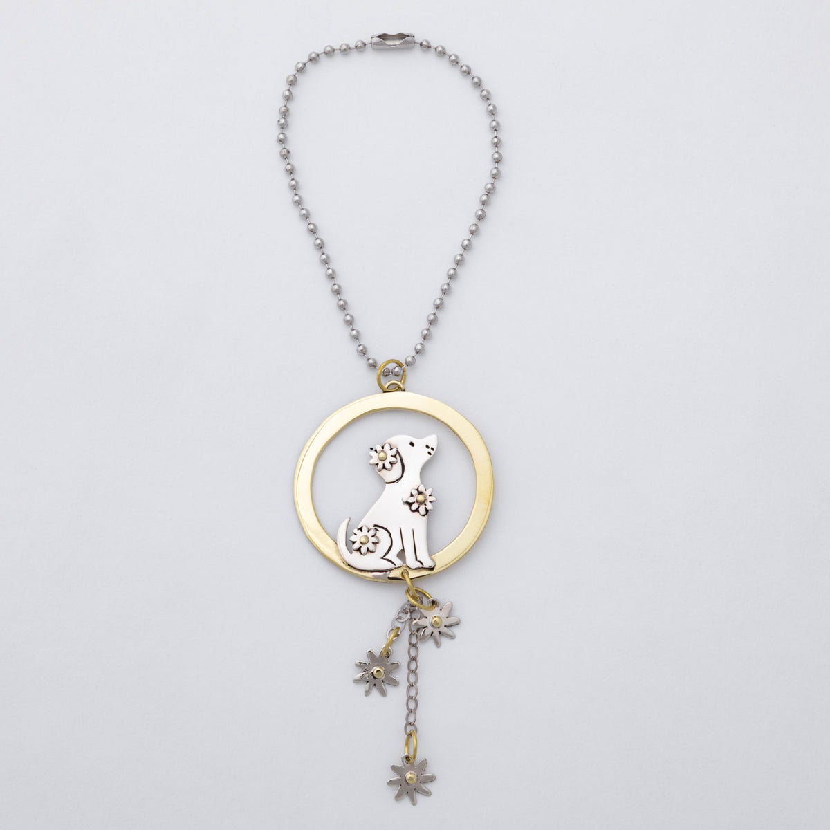 A silver and brass car charm featuring a circular pendant with a gold-toned ring, a silver dog silhouette, and dangling flower charms, shown on a light gray background.