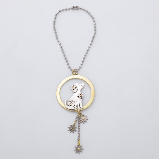 A silver and brass car charm featuring a circular pendant with a gold-toned ring, a silver dog silhouette, and dangling flower charms, shown on a light gray background.