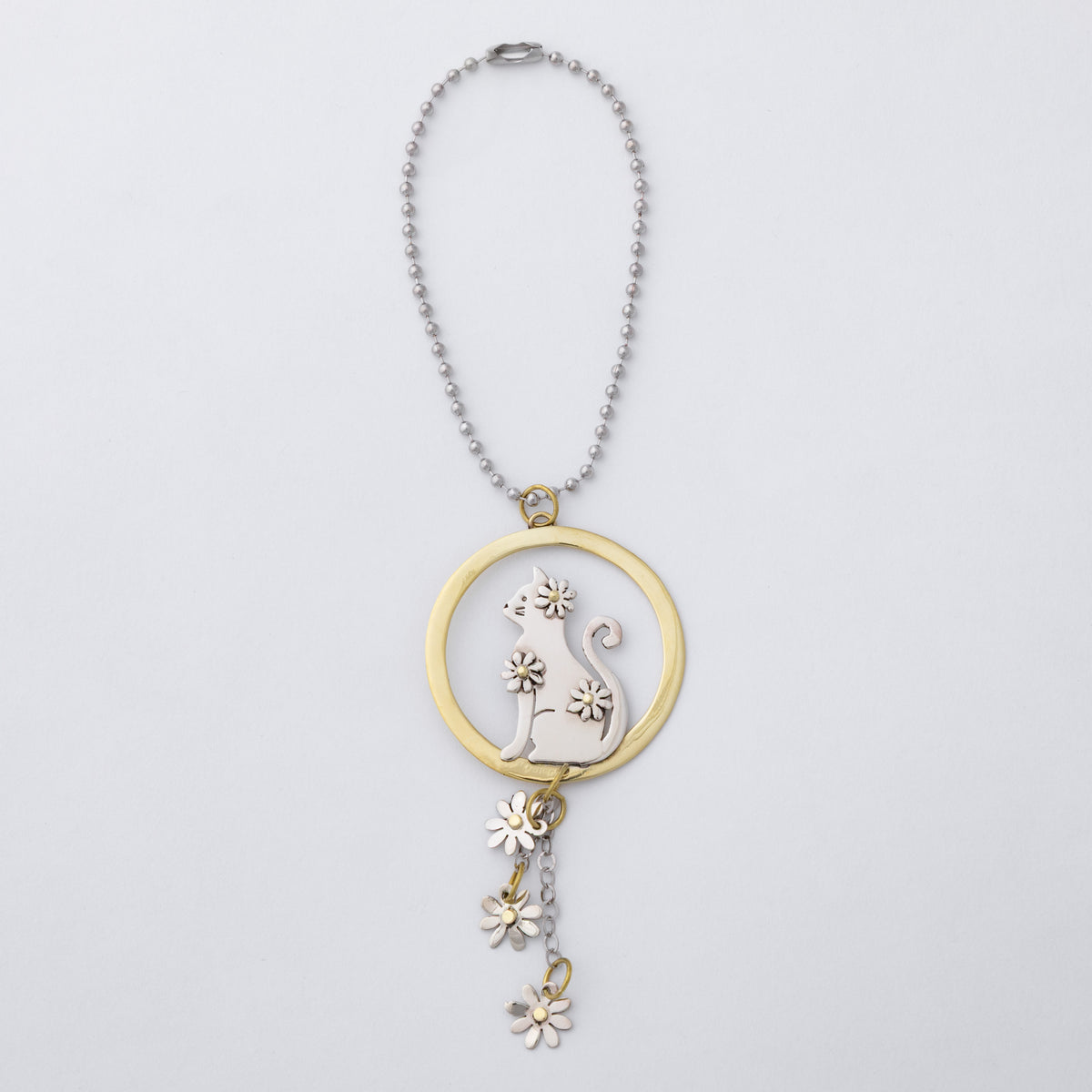 A silver ball chain car charm featuring a circular pendant with a silver cat silhouette and flower details, accented by a gold-tone ring and matching dangling flower charms, shown on a light gray background.