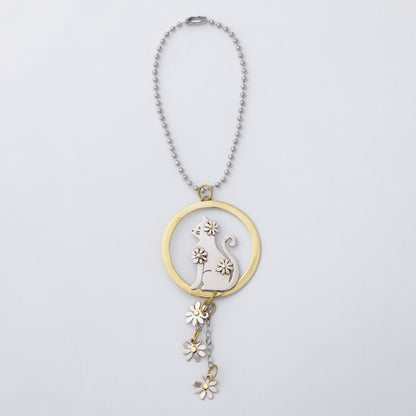 A silver ball chain car charm featuring a circular pendant with a silver cat silhouette and flower details, accented by a gold-tone ring and matching dangling flower charms, shown on a light gray background.