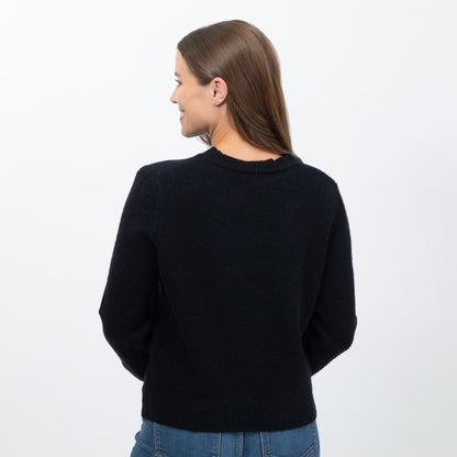 A woman viewed from the back wearing a black knit crewneck sweater and blue jeans against a plain white studio background.
