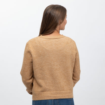 A woman viewed from the back wearing a light tan knit sweater and blue jeans against a plain white background.
