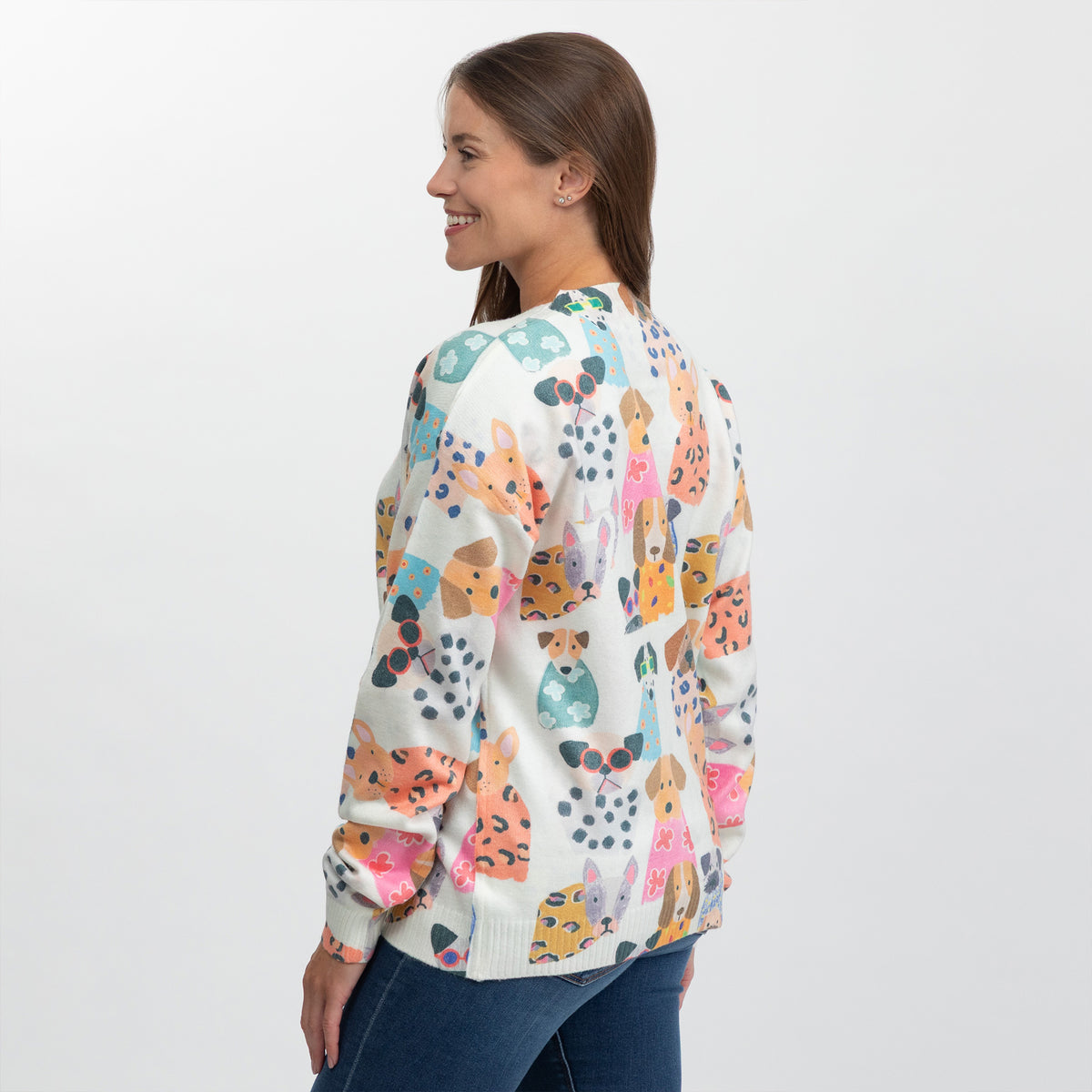 A woman shown from the back wearing a cream-colored knit sweater with a colorful pattern of cartoon dogs, paired with blue jeans, against a plain white studio background.