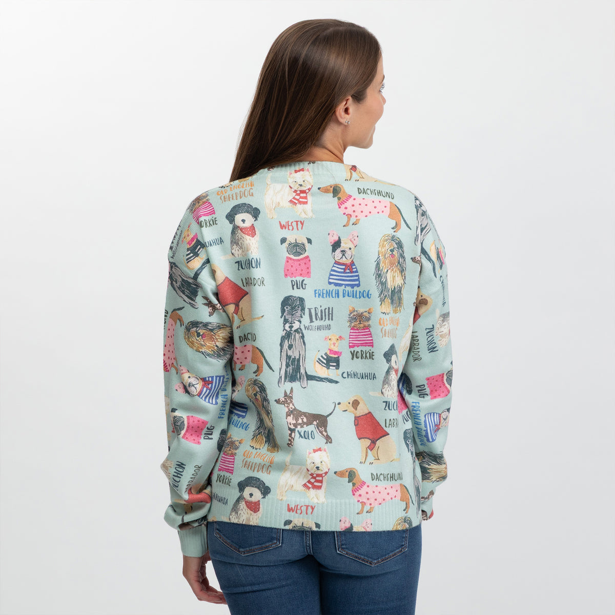 A woman viewed from the back wearing a light blue-green crewneck sweater with a colorful dog-themed graphic print, paired with blue jeans against a plain white background.