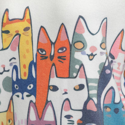 A close-up of a white fabric printed with a dense pattern of stylized cartoon cat heads in multiple colors including orange, yellow, blue, pink, green, and white.
