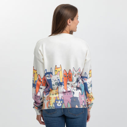 A woman viewed from the back wearing a cream-colored crewneck sweater with a colorful cartoon cat pattern across the lower half and sleeves, paired with blue jeans against a plain white studio background.