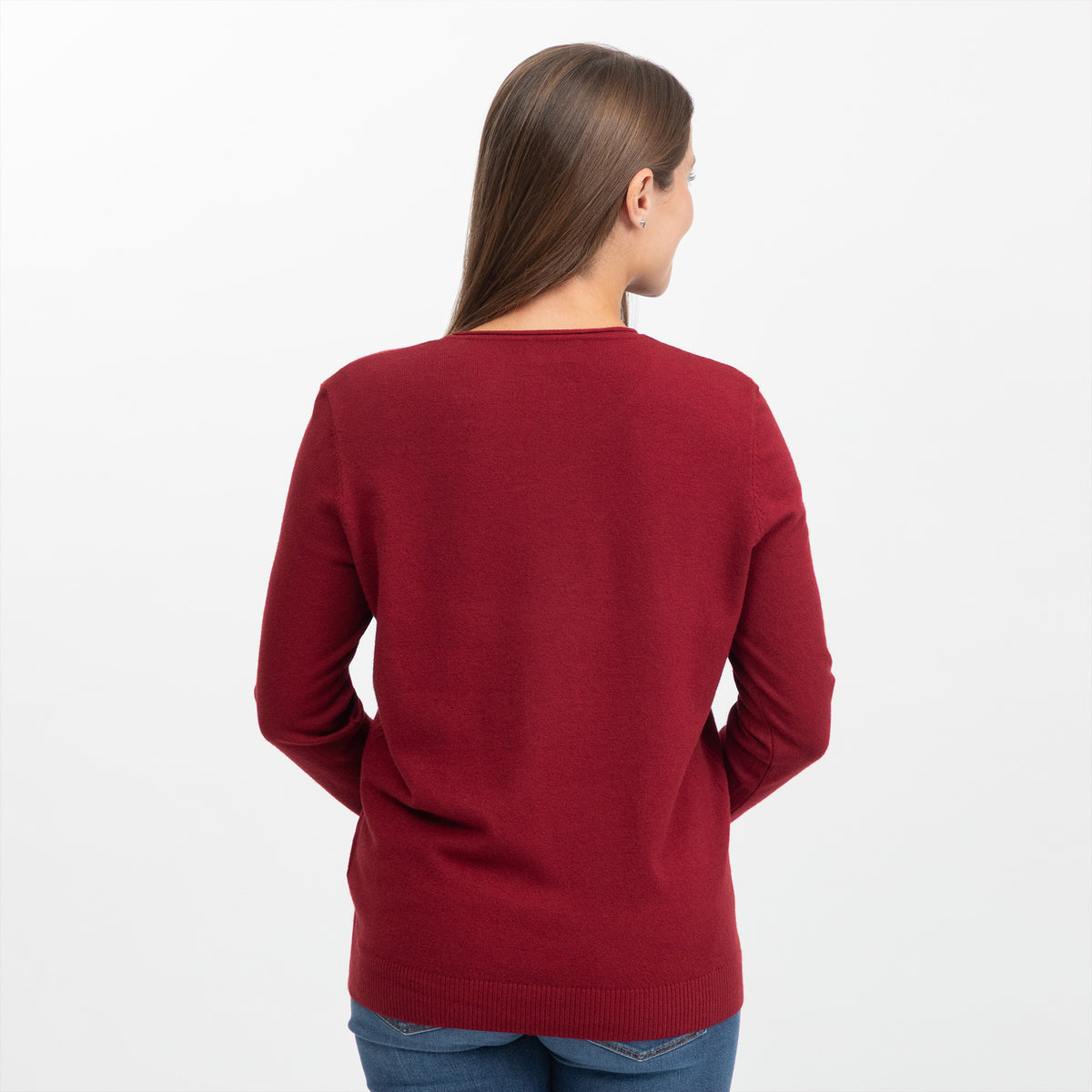 A woman viewed from the back wearing a solid deep red knit sweater and blue jeans against a plain white studio background.
