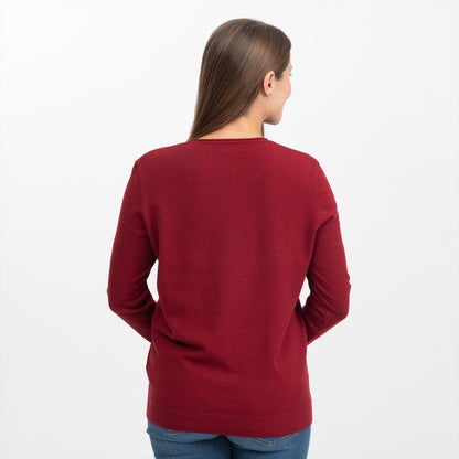 A woman viewed from the back wearing a solid deep red knit sweater and blue jeans against a plain white studio background.