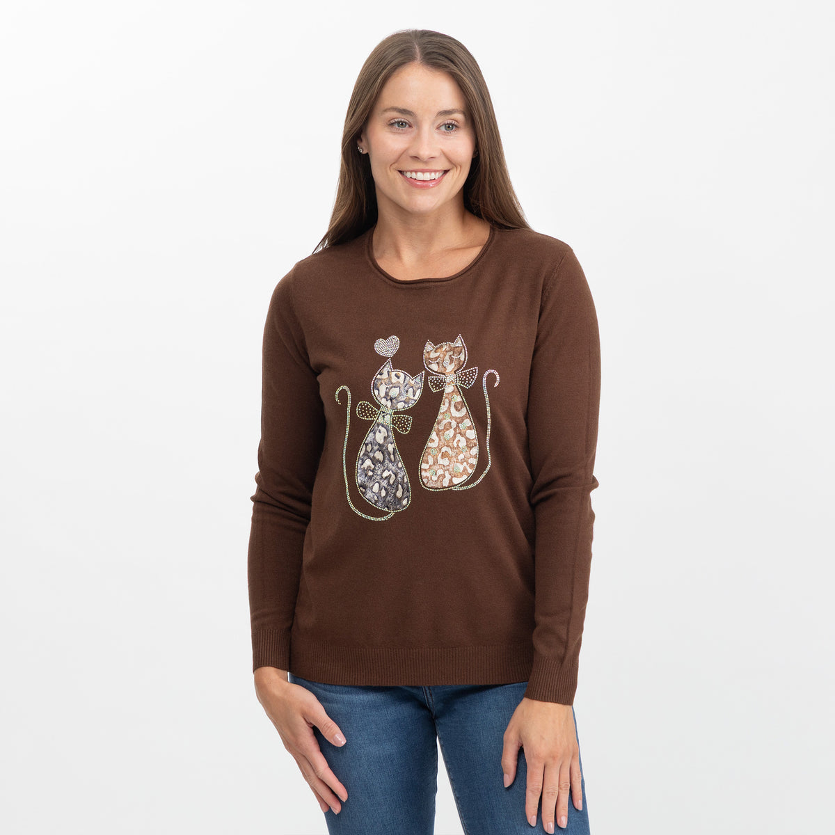 A woman wearing a brown long-sleeve crewneck sweater with a graphic of two patterned cats, paired with blue jeans, against a plain white background.
