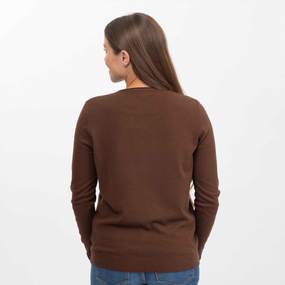 A woman viewed from the back wearing a solid brown long-sleeve knit sweater and blue jeans against a plain white studio background.