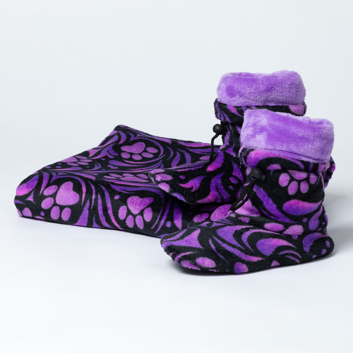 Purple and black fleece booties with a paw print pattern and plush purple trim, shown with a matching zippered pouch on a light gray background.