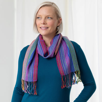 A woman wearing a teal shirt and a multicolored, striped alpaca fiber scarf with fringes.
