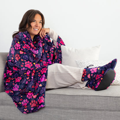 Woman sitting on a couch with a colorful paw print and heart blanket and matching fleece slippers.