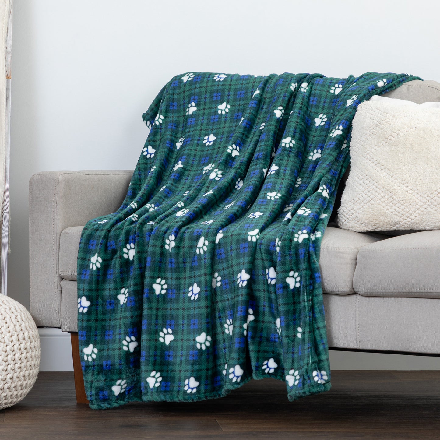A green plaid throw blanket with white paw prints draped over a light gray sofa in a living room setting.