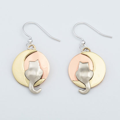 Pair of cat-shaped earrings with brass and copper moon designs on a light gray background