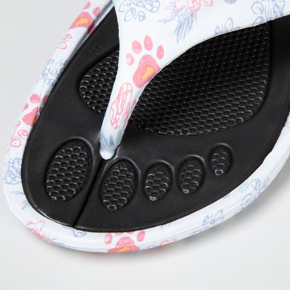 A detail image of waves and marble paws print design EVA flip flops on a white background, showing the textured footbed of the flip flops, the waves and marble paws print is on white background and the textured foot bed is black