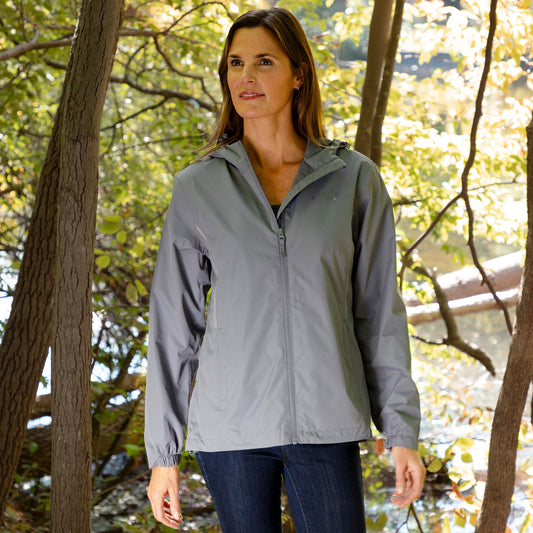 Woman wearing a gray rain jacket standing in an outdoor setting with trees in the background