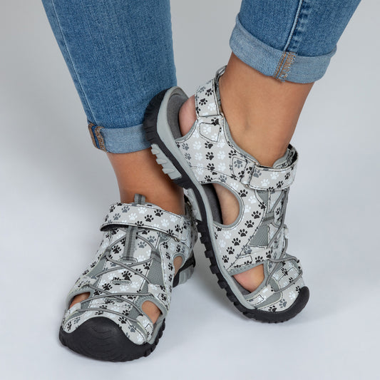 Gray sandals with a paw print design, worn by a person in jeans.