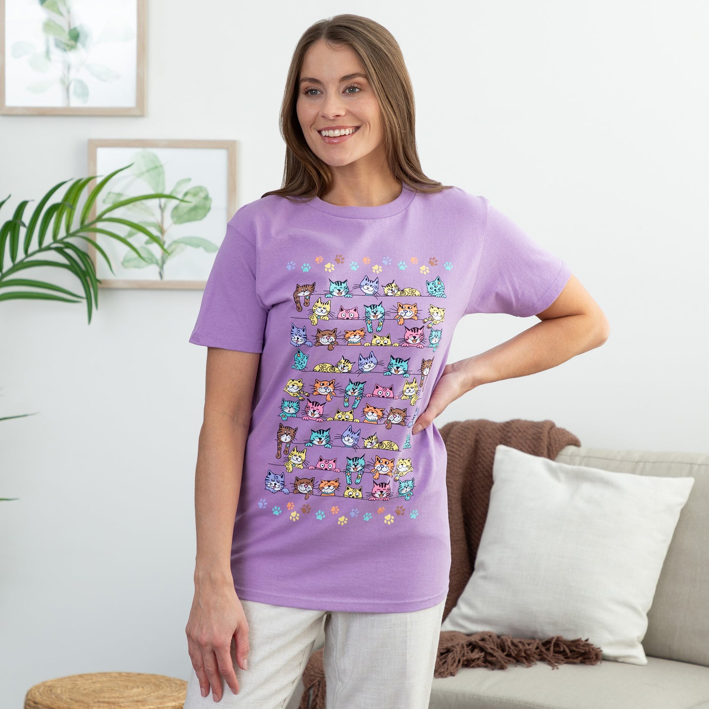 Woman wearing a purple t-shirt with colorful cat illustrations in a living room setting.