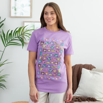 Woman wearing a purple t-shirt with colorful cat pattern in a room with a plant and couch.