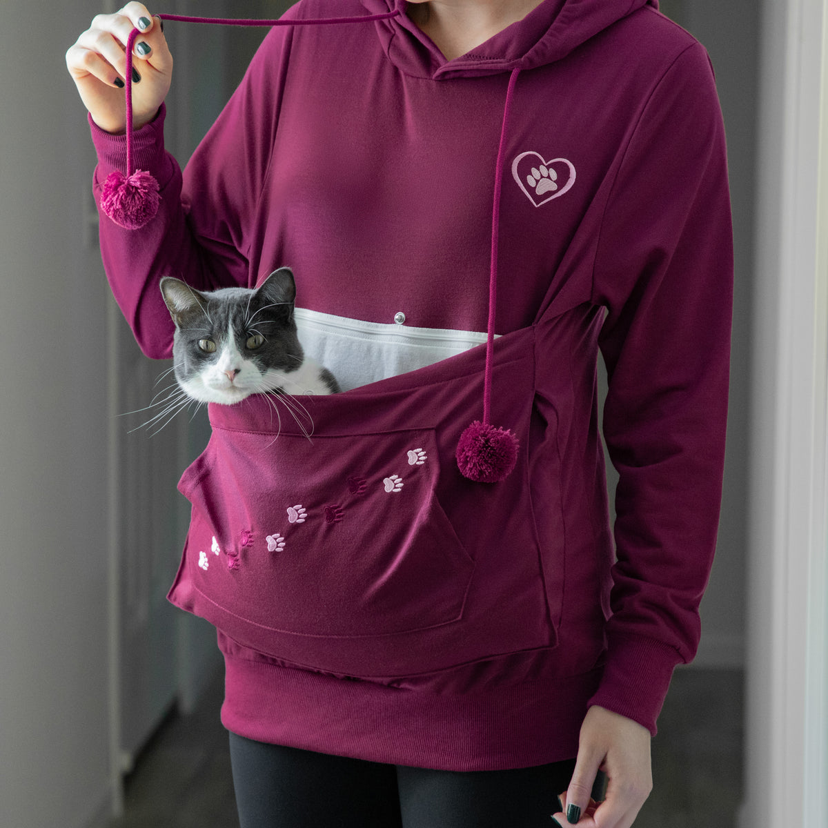 A person wearing a maroon hoodie with a cat in the front pocket.